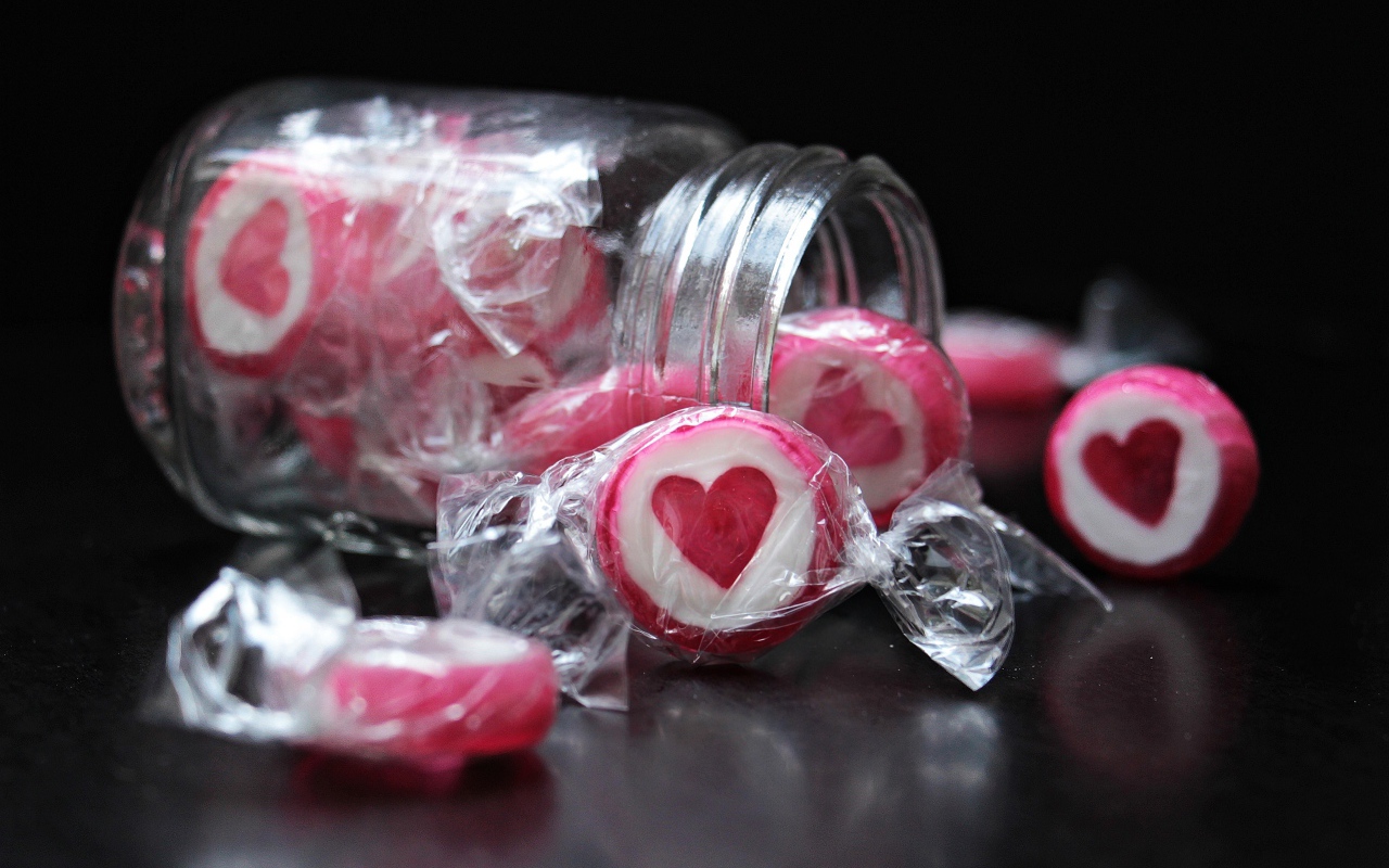 Конфеты с сердцем в стеклянной банке на черном фоне