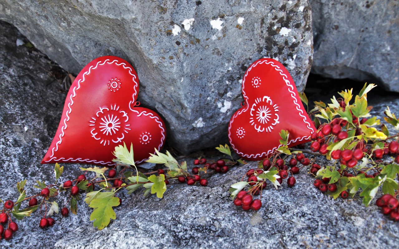 Два сердца лежат у камня с красными ягодами