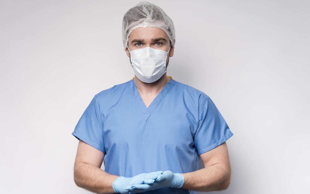 Мужчина врач в маске и перчатках на сером фоне