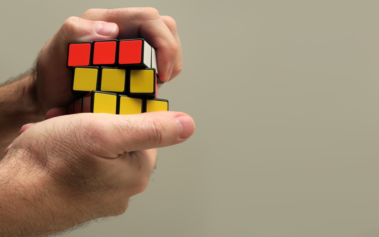 Кубик Рубика в руках мужчины на сером фоне