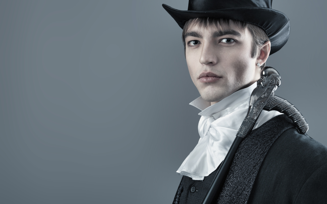 Красивый молодой человек в черном цилиндре и фраке на сером фоне