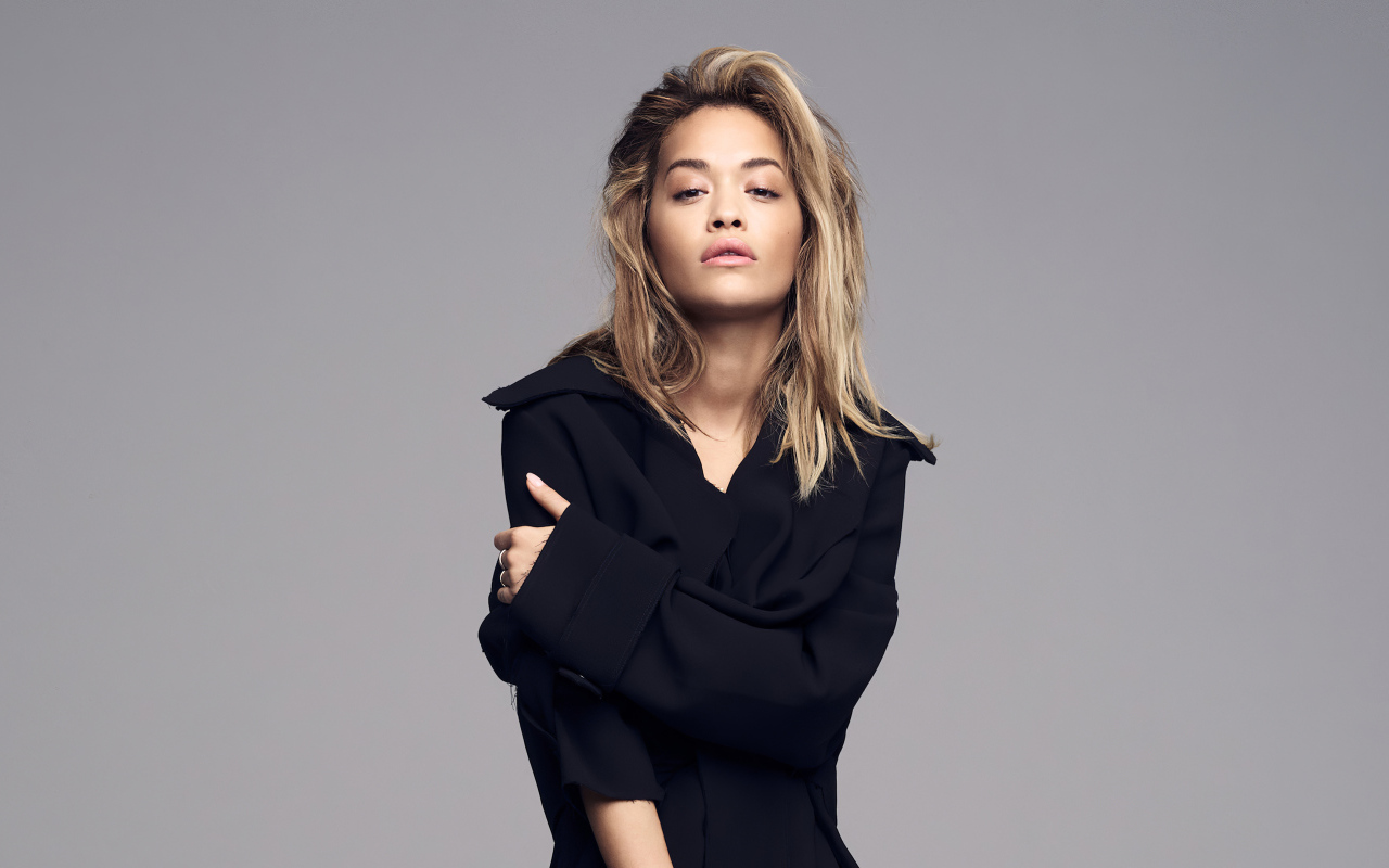 Певица Рита Ора в черном наряде на сером фоне