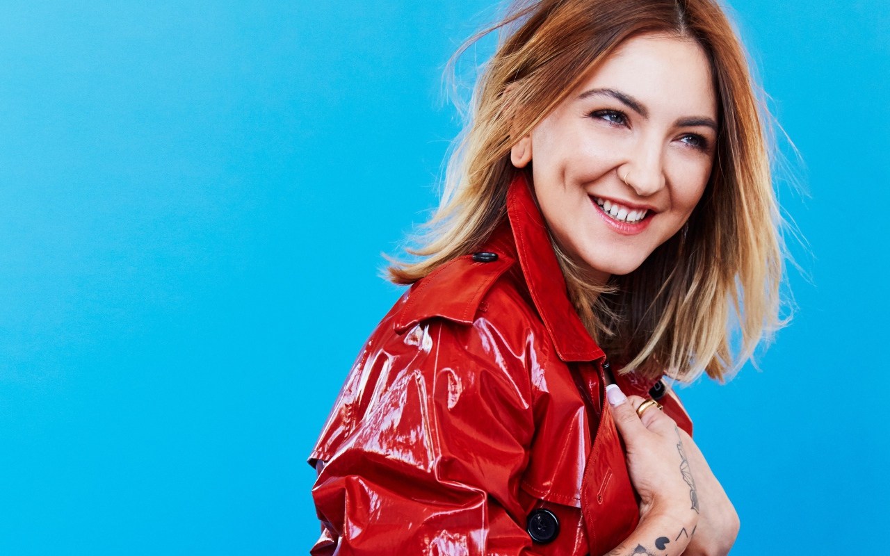Smiling singer Julia Michaels in a red jacket on a blue background