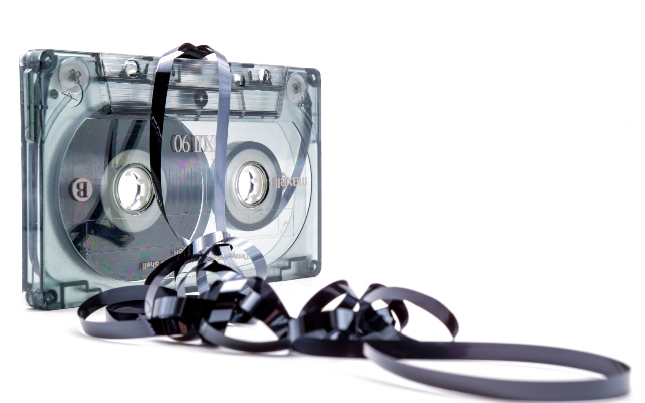 Магнитофонная кассета в размотанной пленкой на белом фоне