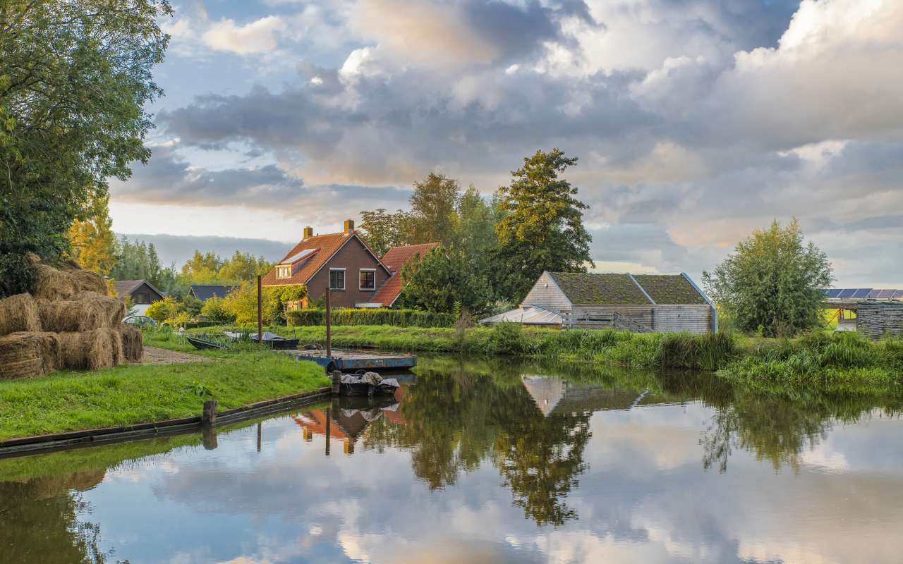 Дома отражаются в реке под небом с белыми облаками