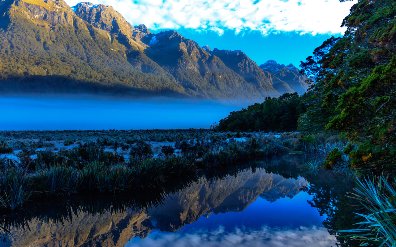 Горы и небо отражаются в голубой воде озера 