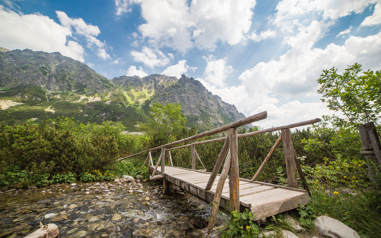 Старый деревянный мост через речку на фоне гор