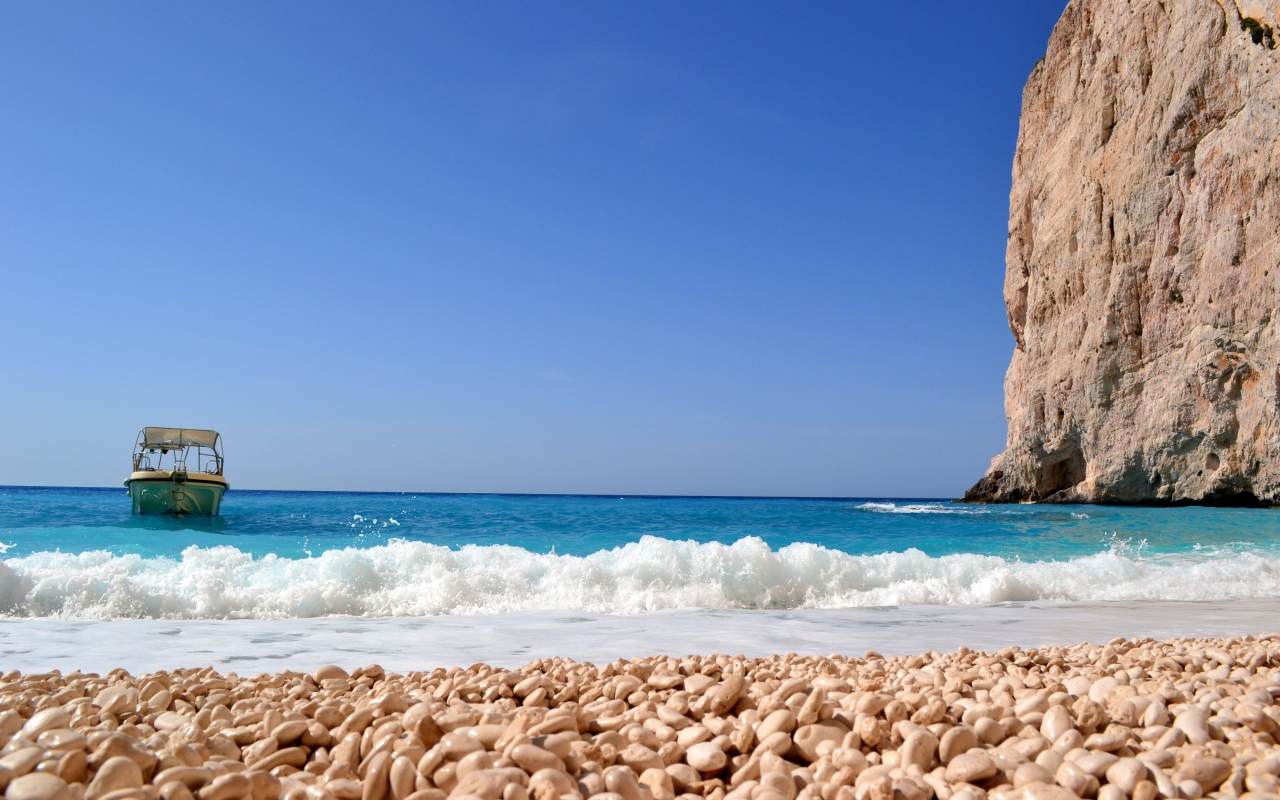 Красивая голубая вода с белыми волнами на пляже с галькой 