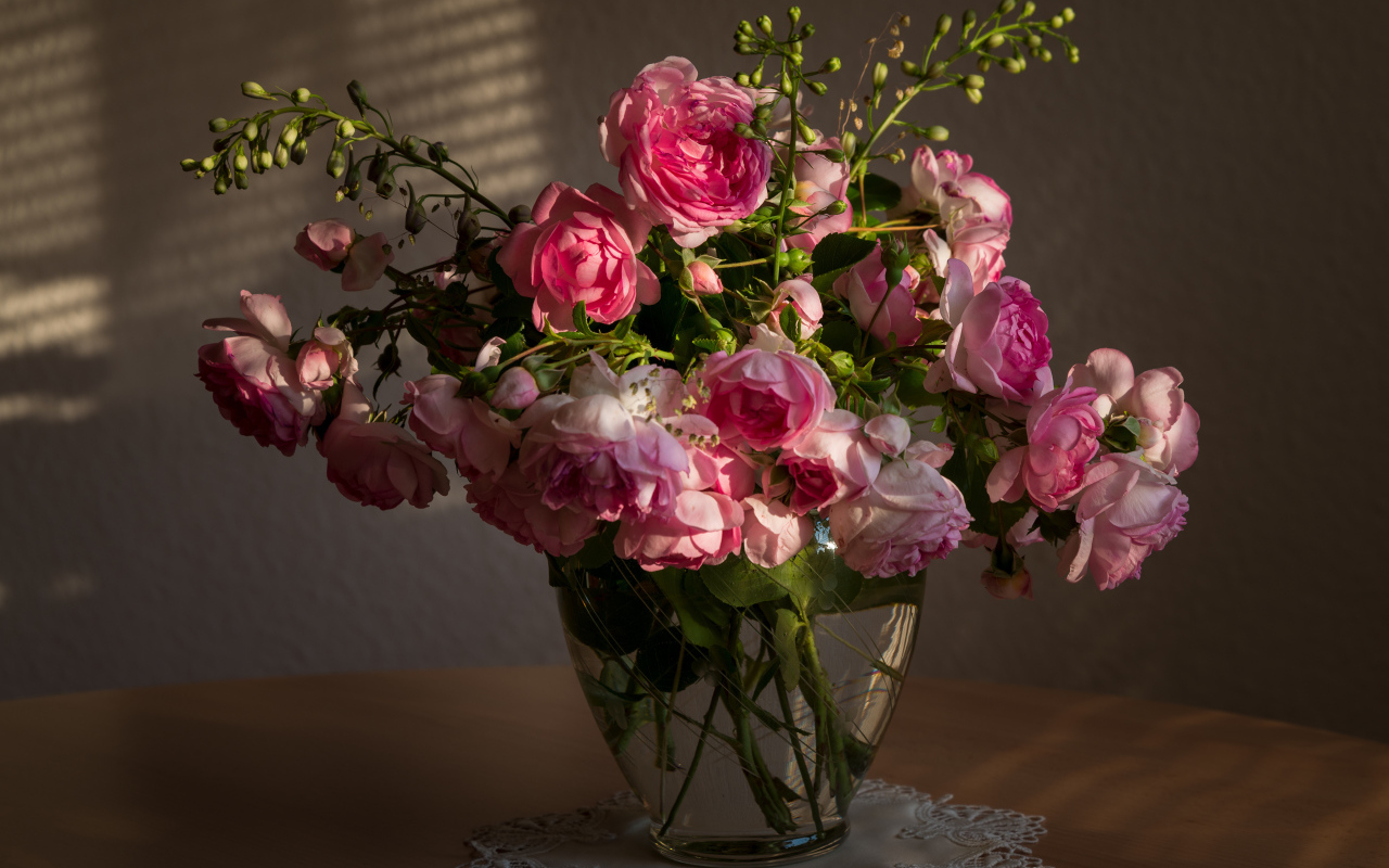 Букет розовых роз в стеклянной вазе не столе в лучах солнца 