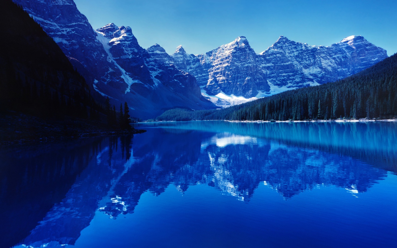 Высокие заснеженные горы отражаются в воде озера 