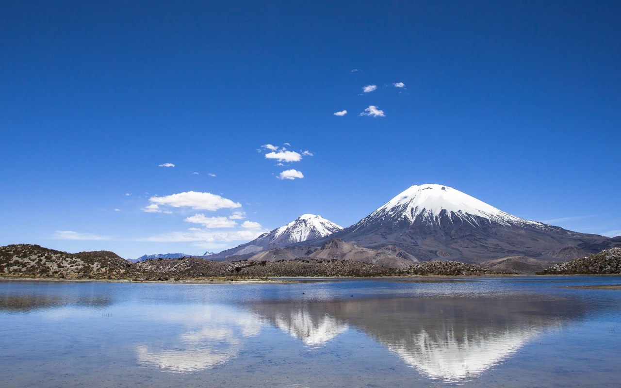 Заснеженные вершины гор под голубым небом отражаются в воде 