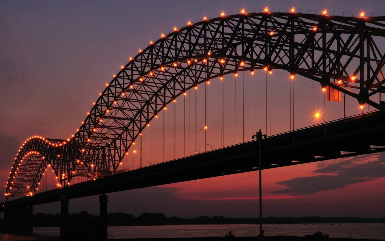 Арки на железном мосту с фонарями ночью через реку 