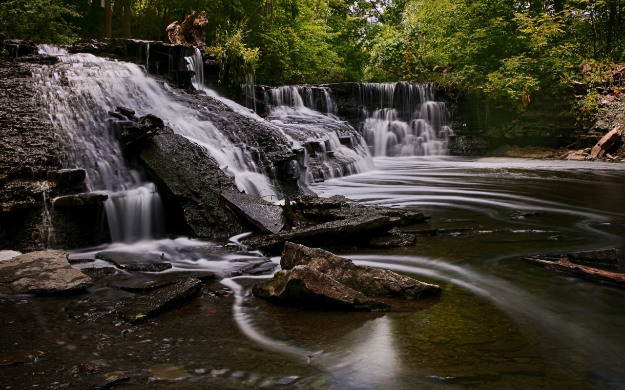 Быстрая вода стекает по камням водопада в парке 