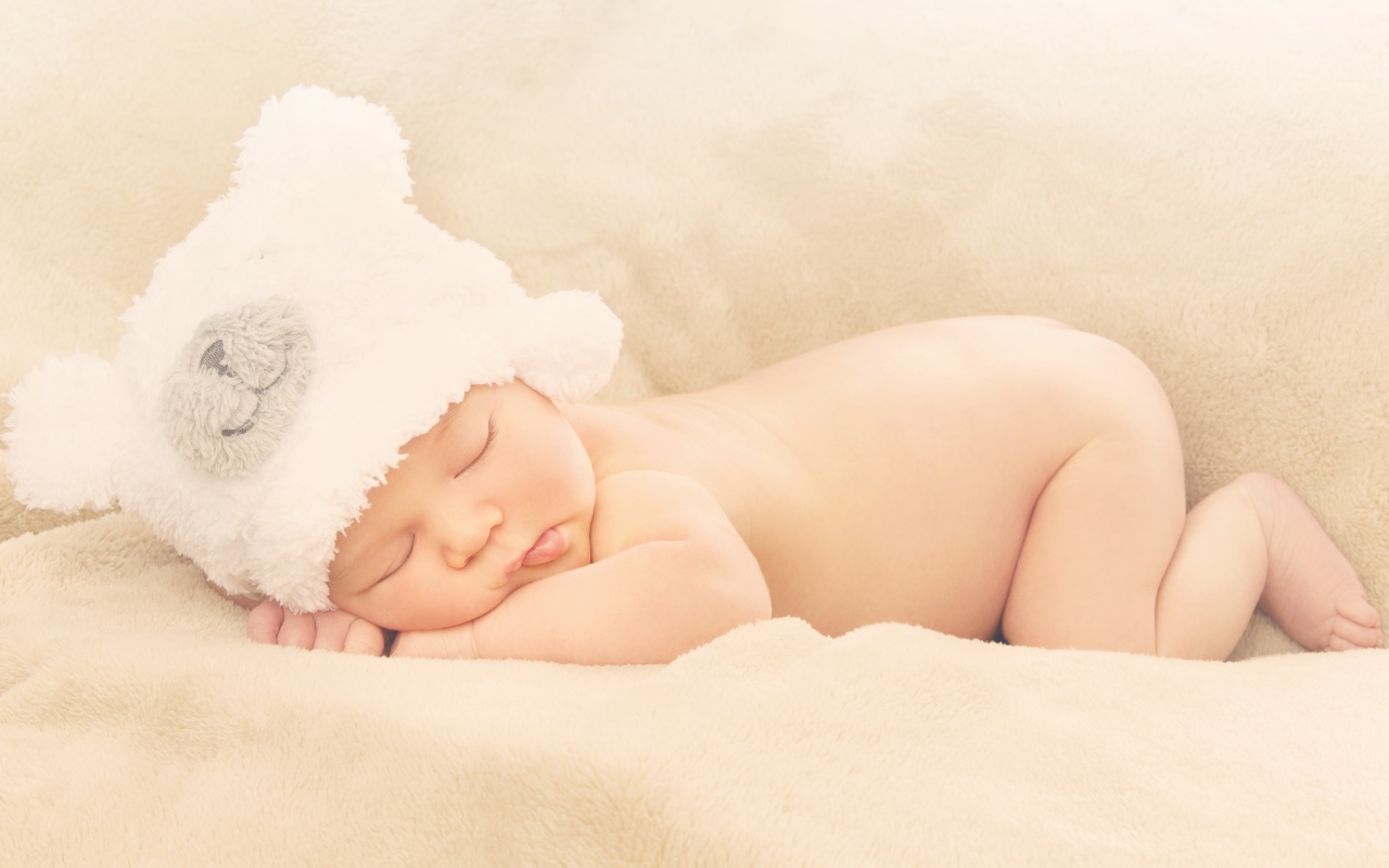 Грудной ребенок с белой шапке спит на кровати