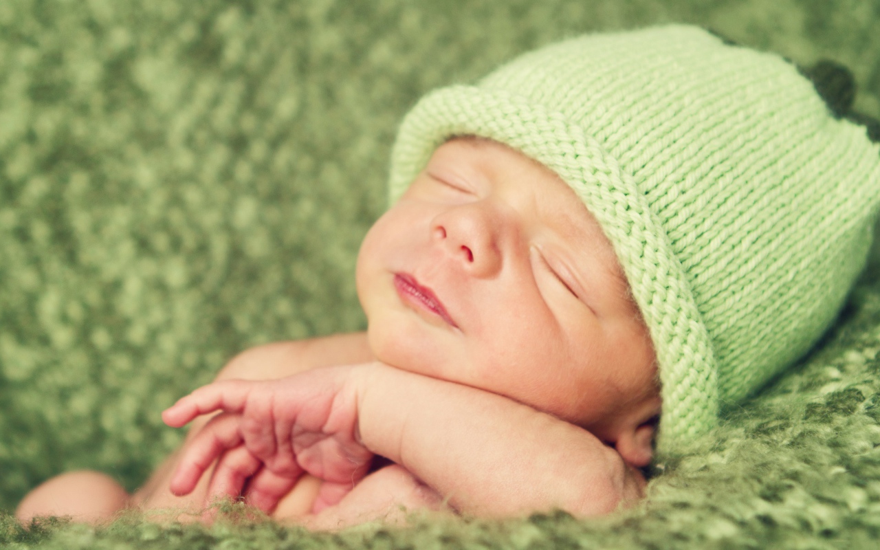 Зеленая вязаная шапка на голове у спящего ребенка 