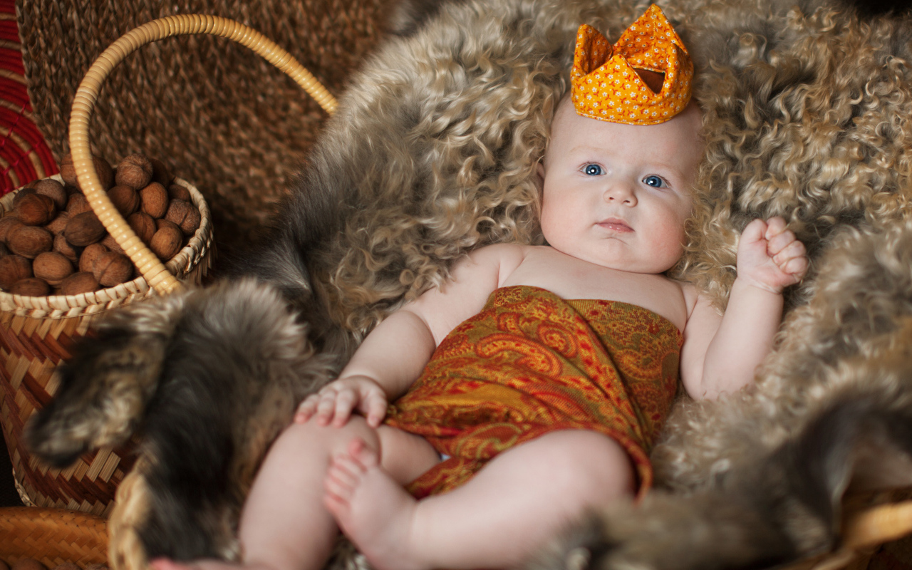 Маленький грудной ребенок в короне лежит в корзине 