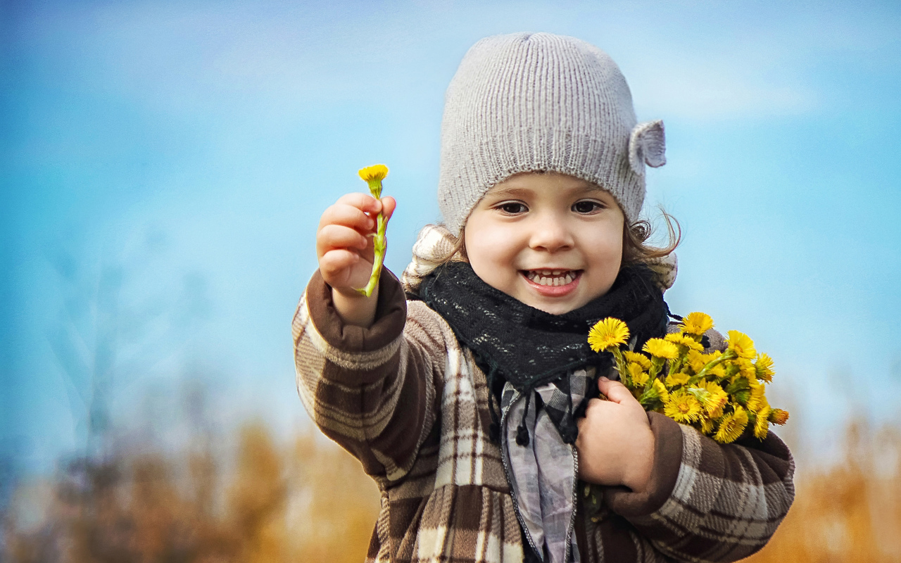 Маленькая девочка в шапке с желтыми цветами в руке