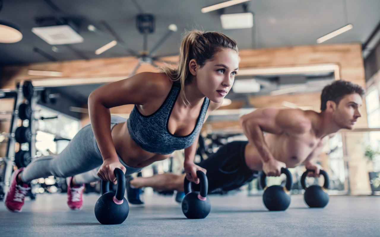 Парень и девушка занимаются с гирями в спортзале 