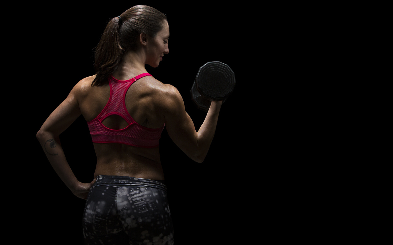 Девушка качает руки гантелей на черном фоне 