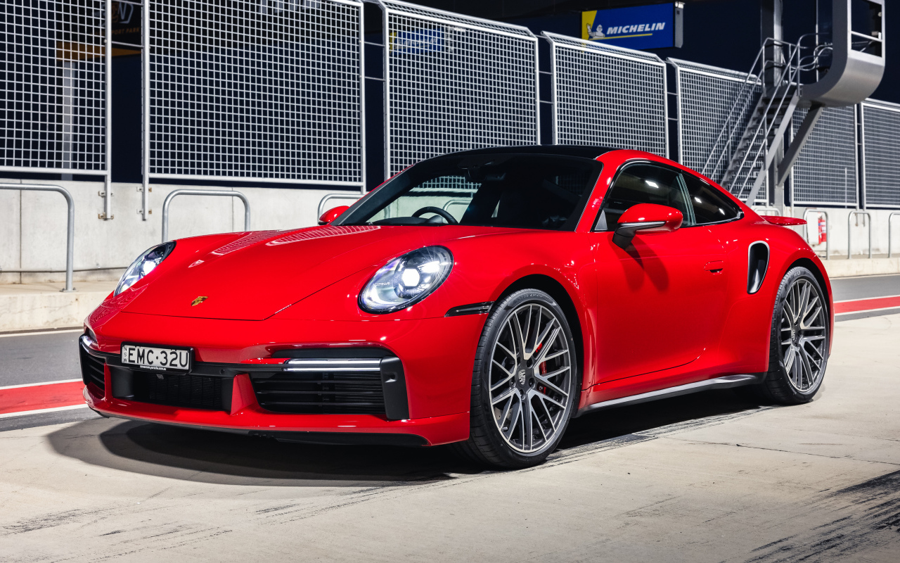 Красный автомобиль Porsche 911 Turbo 2021 года на стадионе