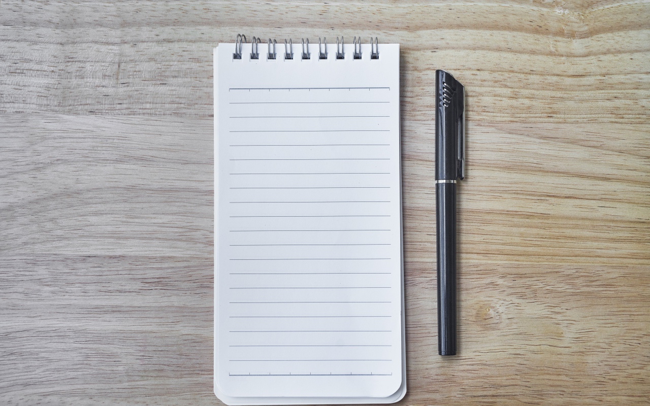 Авторучка и блокнот лежат на деревянном столе