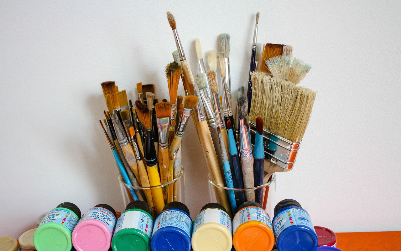 Много кисточек и разноцветные краски у стены