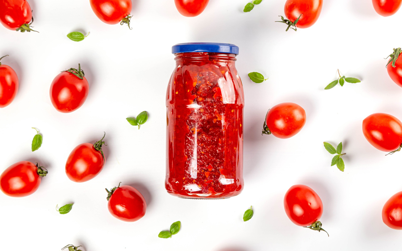 Банка аджики на белом фоне с помидорами