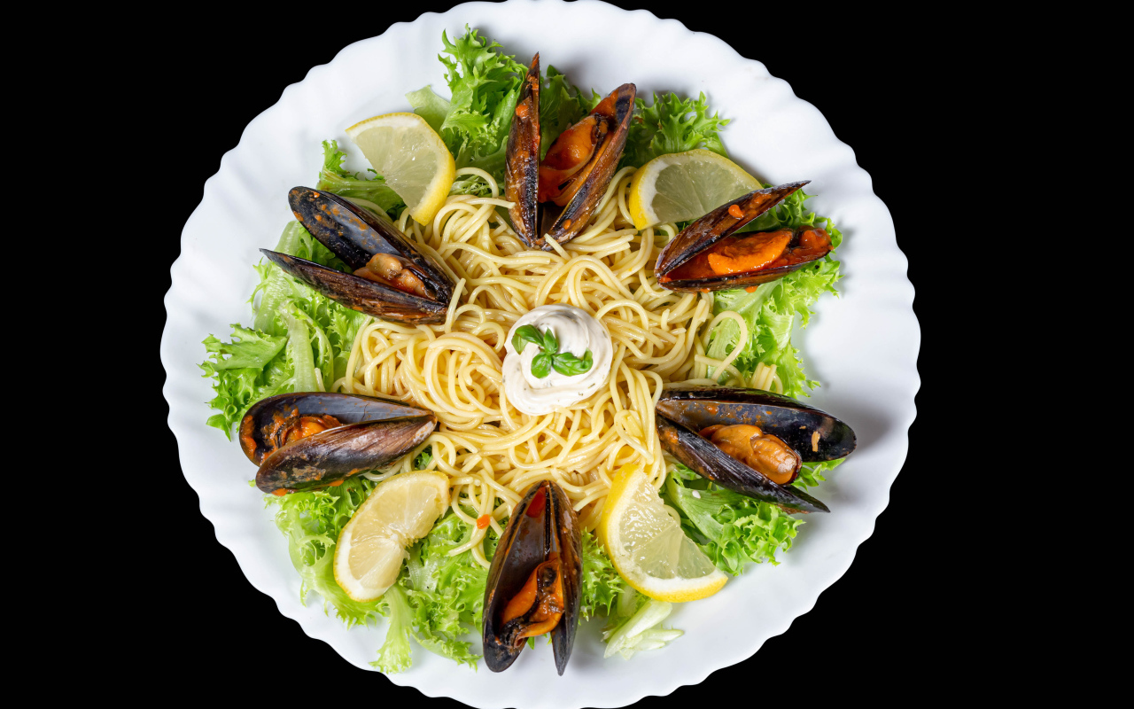 Спагетти с мидиями и листьями салата на белой тарелке