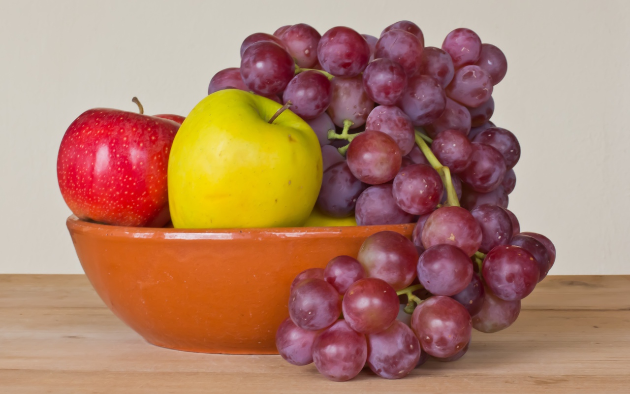 Яблоки и розовый виноград в тарелке на столе 