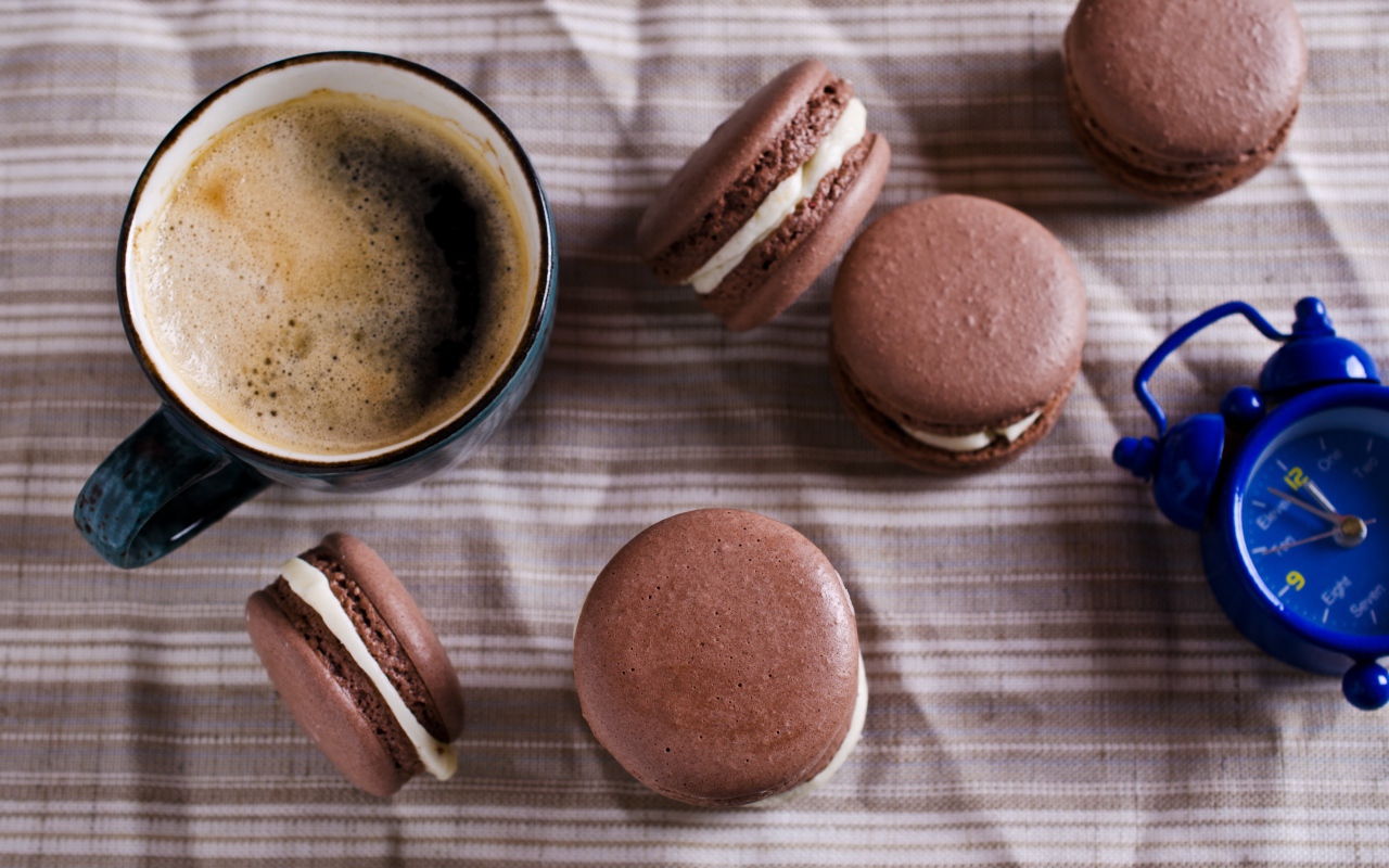 Чашка кофе на столе с десертом макарун и будильником