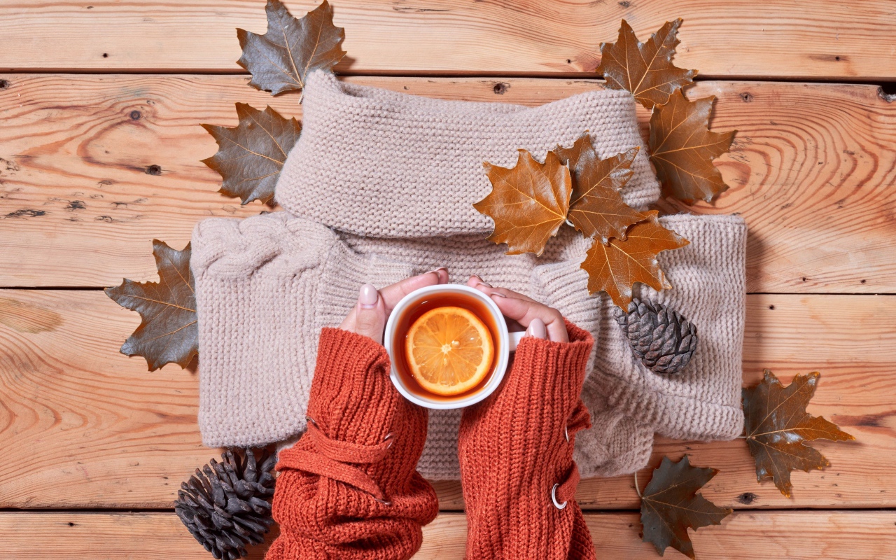 Чашка горячего чая с лимоном в руках на столе с теплым свитером