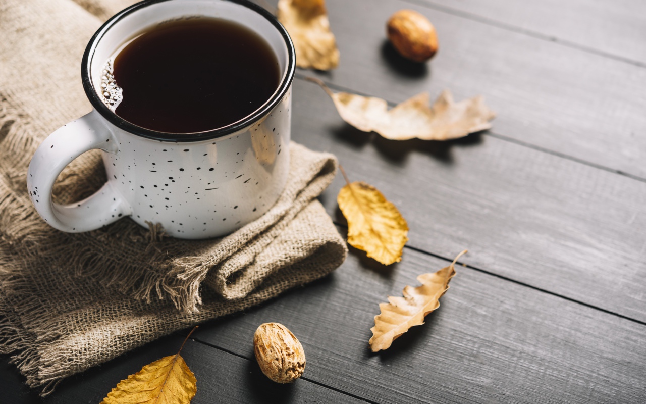 Кружка кофе на столе с листьями и пледом