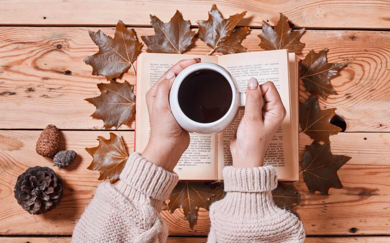 Чашка кофе в руках на столе с книгой и листьями
