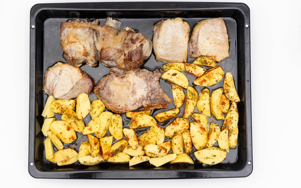 Pork on a baking sheet with potatoes on a white plate