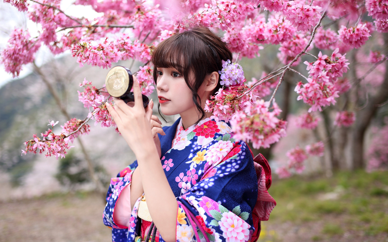 Девушка в кимоно стоит у куста сакуры