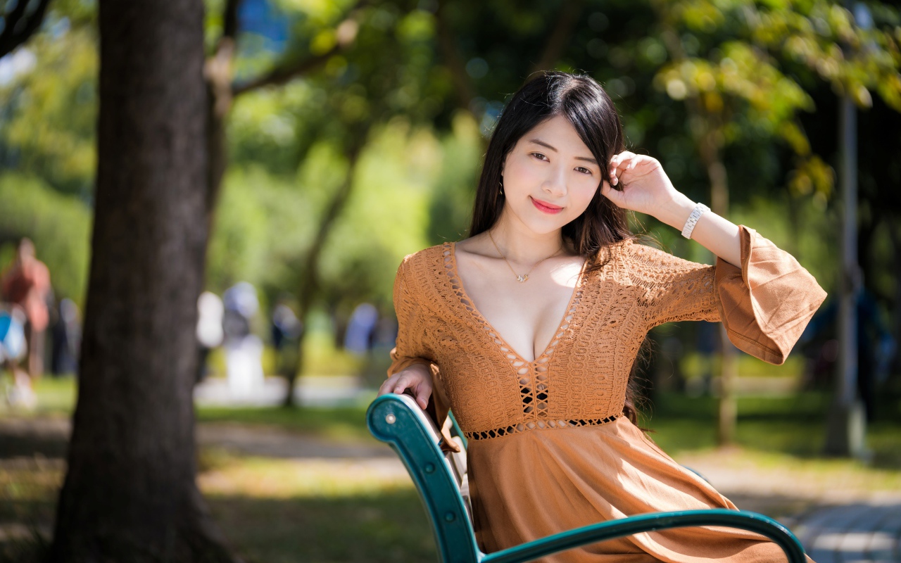 Молодая девушка азиатка в коричневом платье сидит на лавке