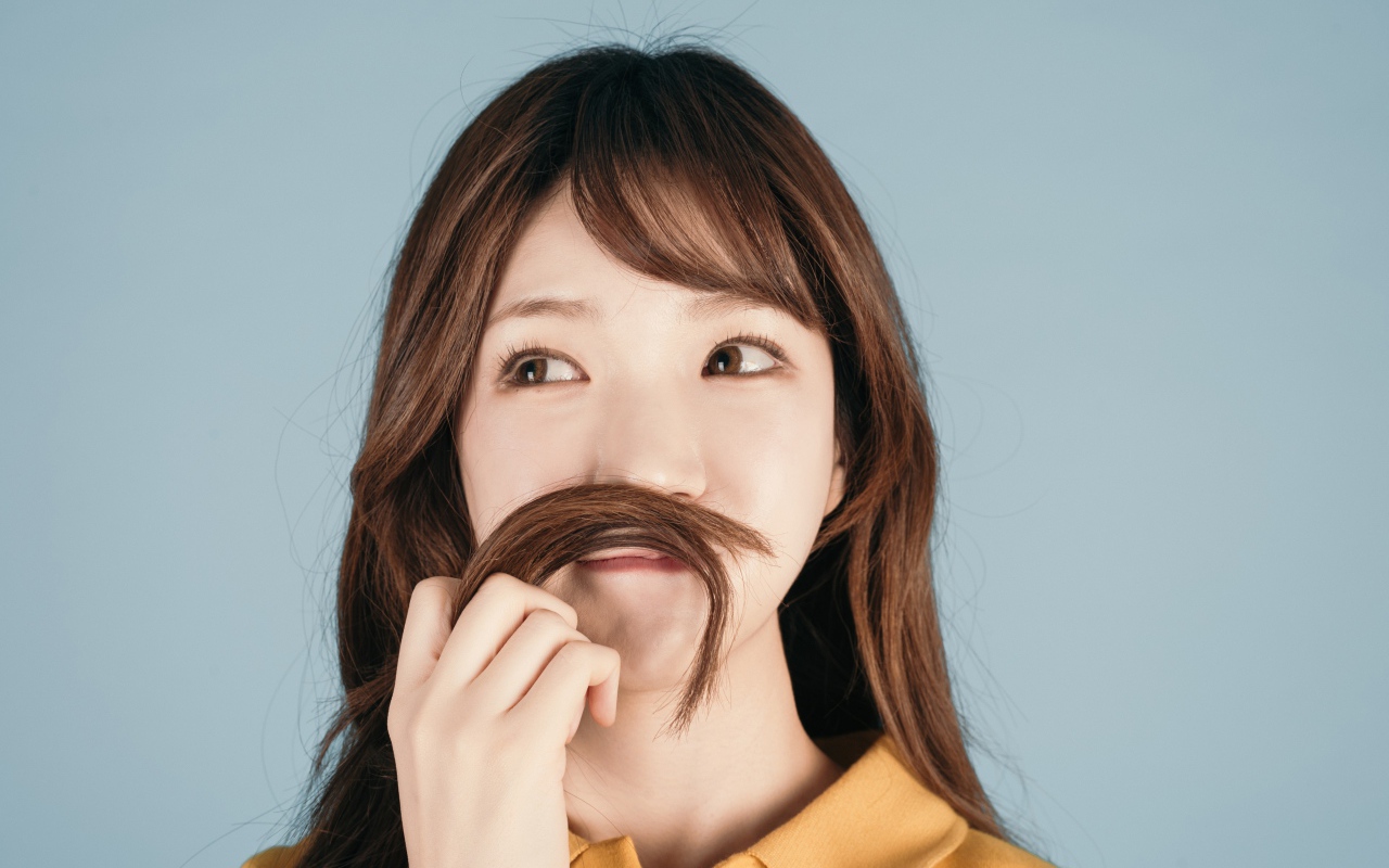 Девушка азиатка закрыла лицо волосами на сером фоне 