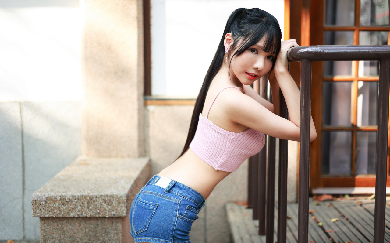 Девушка азиатка в коротких шортах стоит у перил 