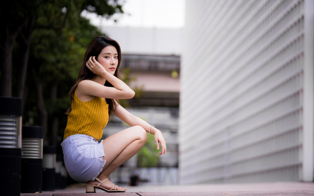 Девушка азиатка сидит на корточках у стены