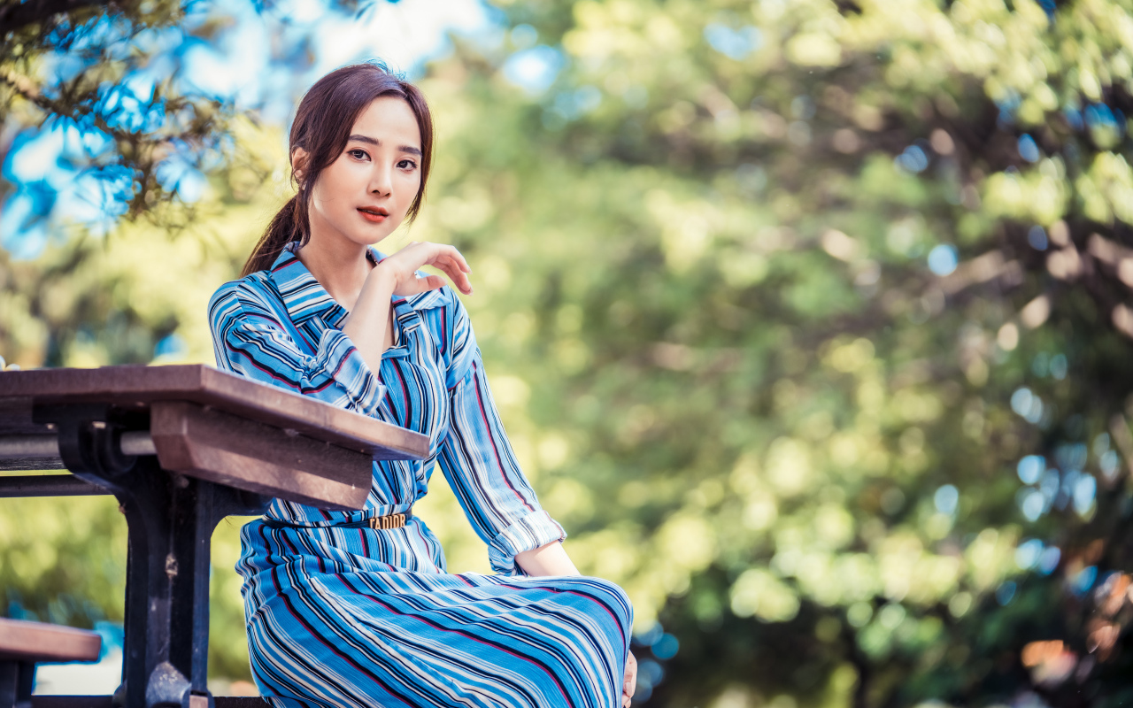 Красивая девушка азиатка в платье  за столом в парке 