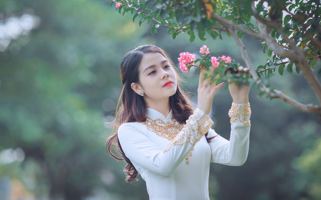 Красивая азиатка в белом платье у ветки с розовыми цветами