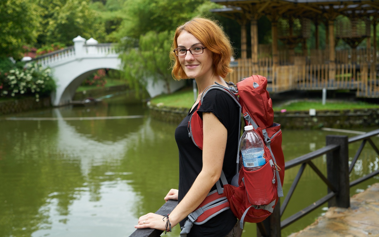 Рыжеволосая девушка с рюкзаком у пруда 