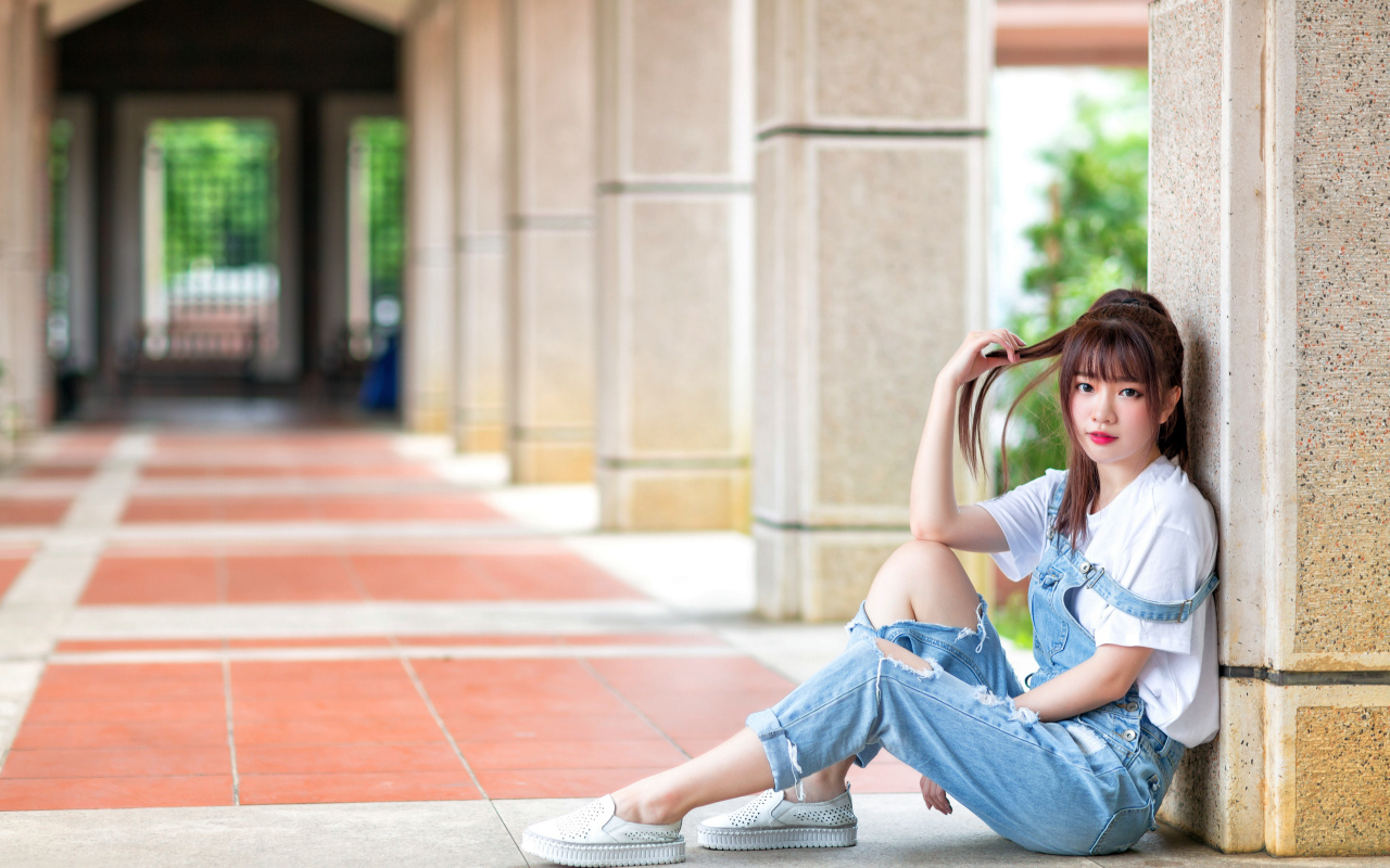 Грустная девушка азиатка сидит у колонны