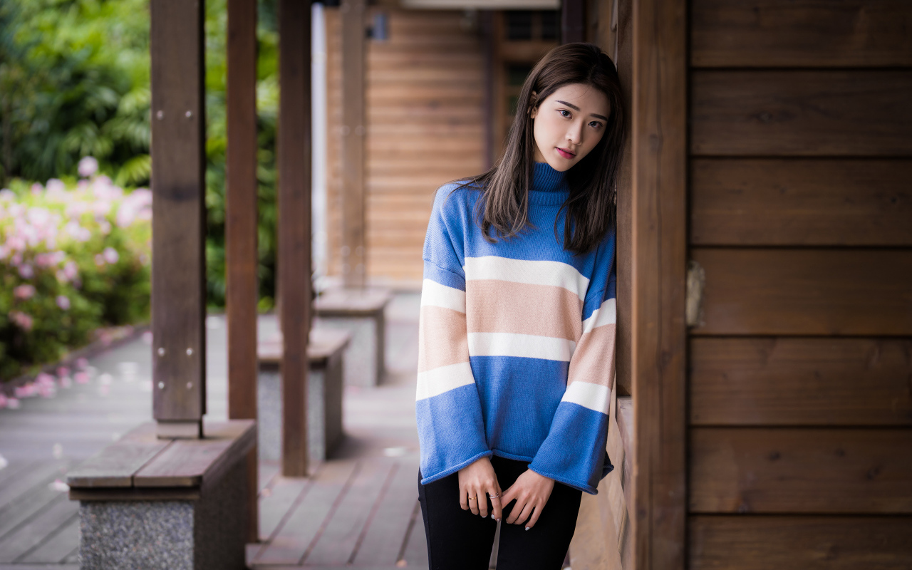 Грустная девушка азиатка в свитере у стены 