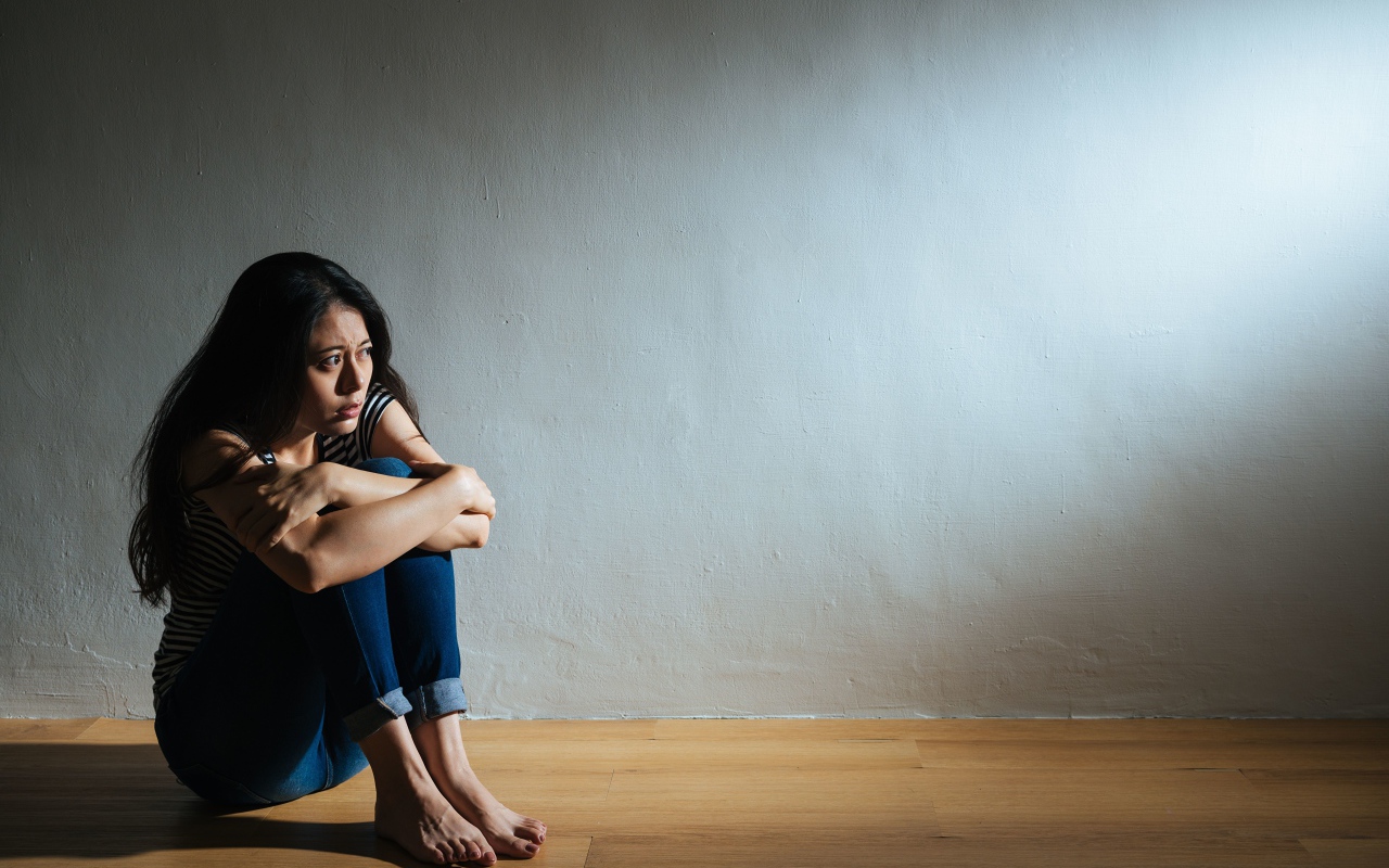 Испуганная девушка азиатка сидит у стены