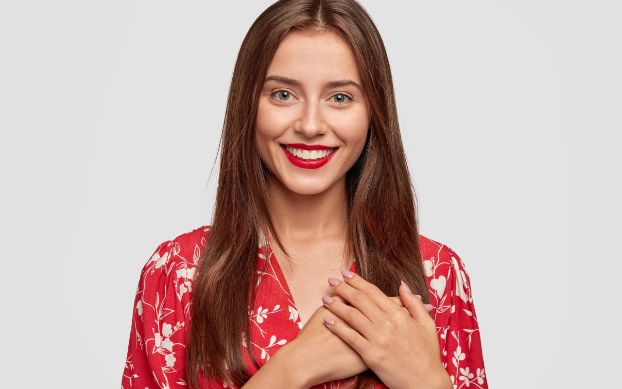 Улыбающаяся девушка с руками на сердце на сером фоне