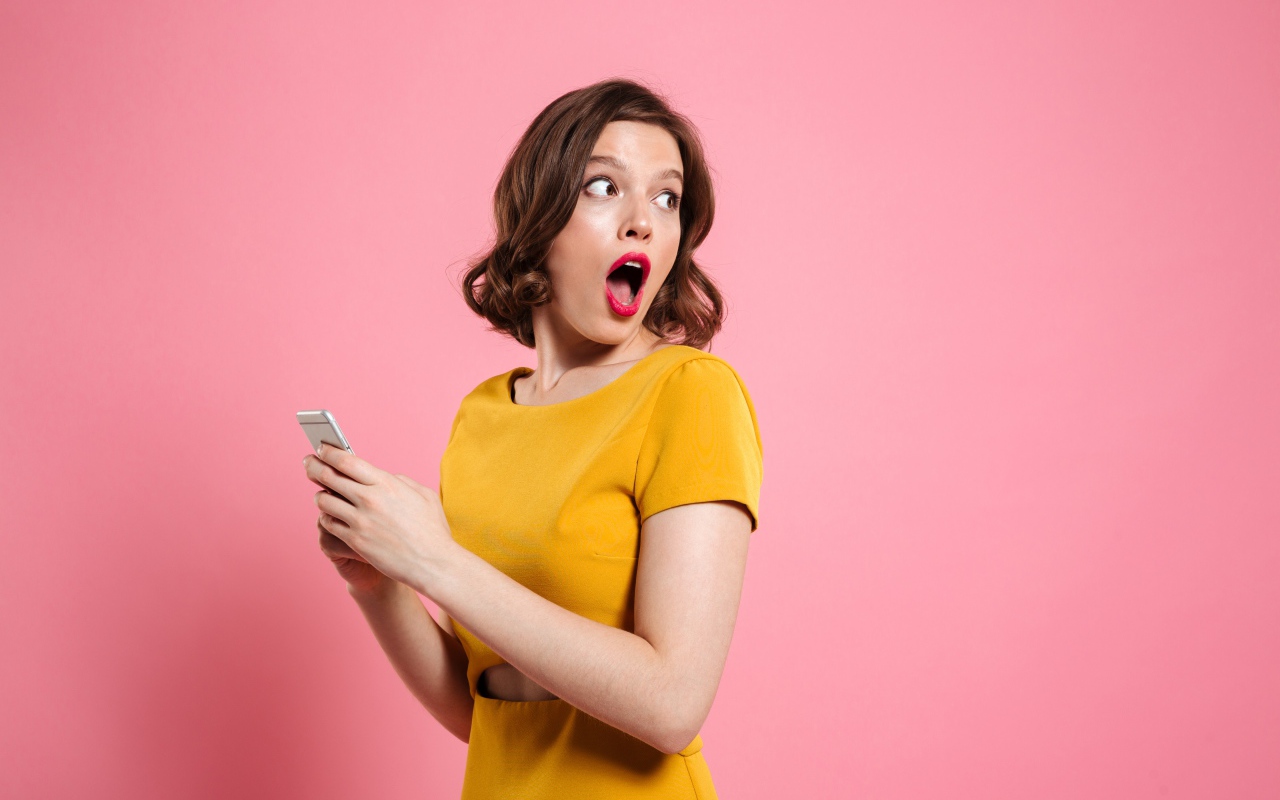 Удивленная девушка с телефоном в руках на розовом фоне