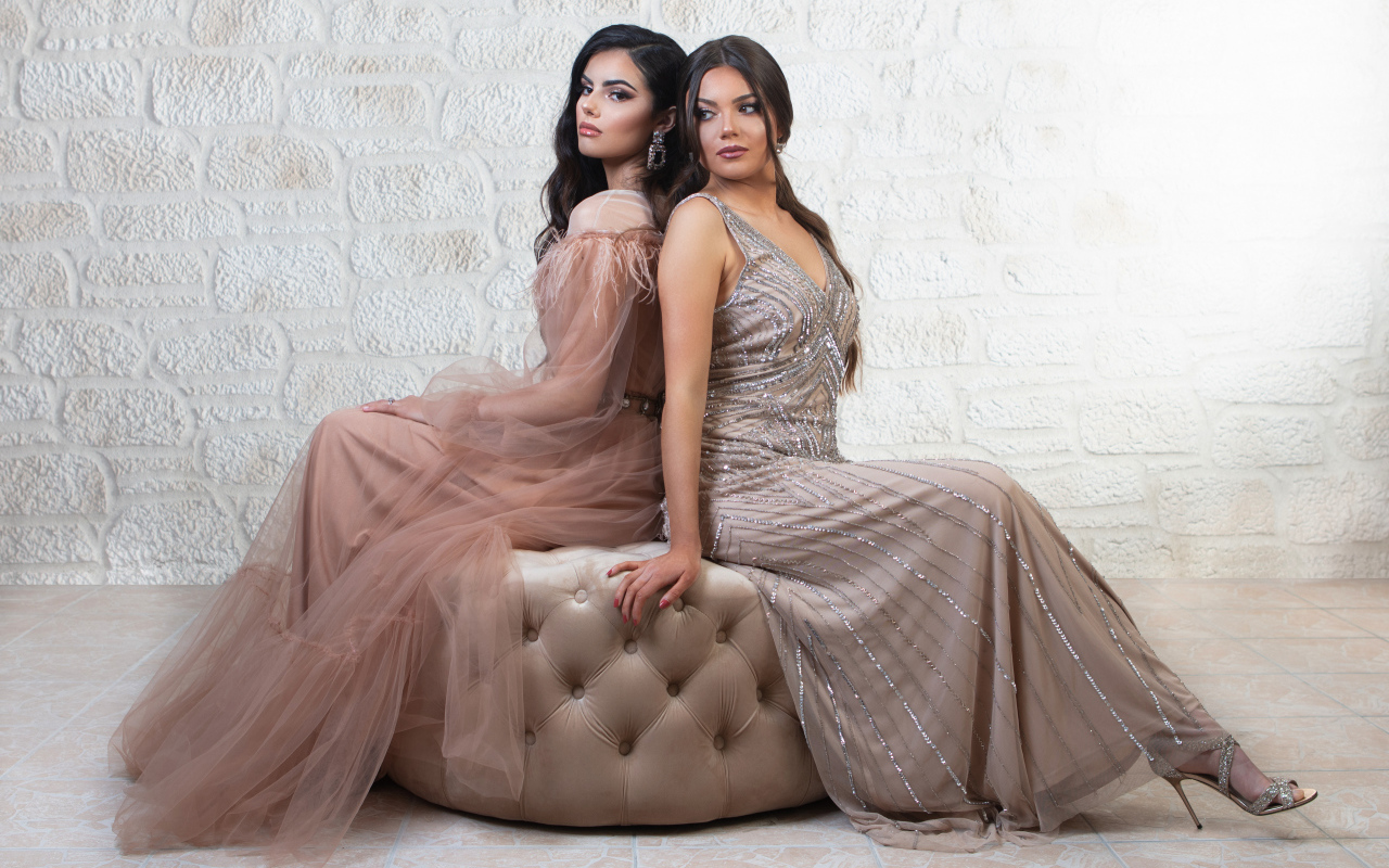 Две девушки в красивых платьях сидят на диване 