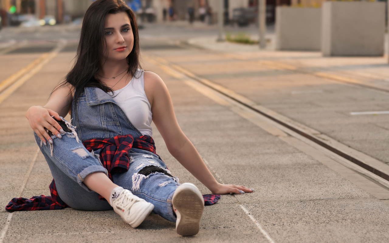 Молодая девушка в джинсовом наряде сидит на асфальте