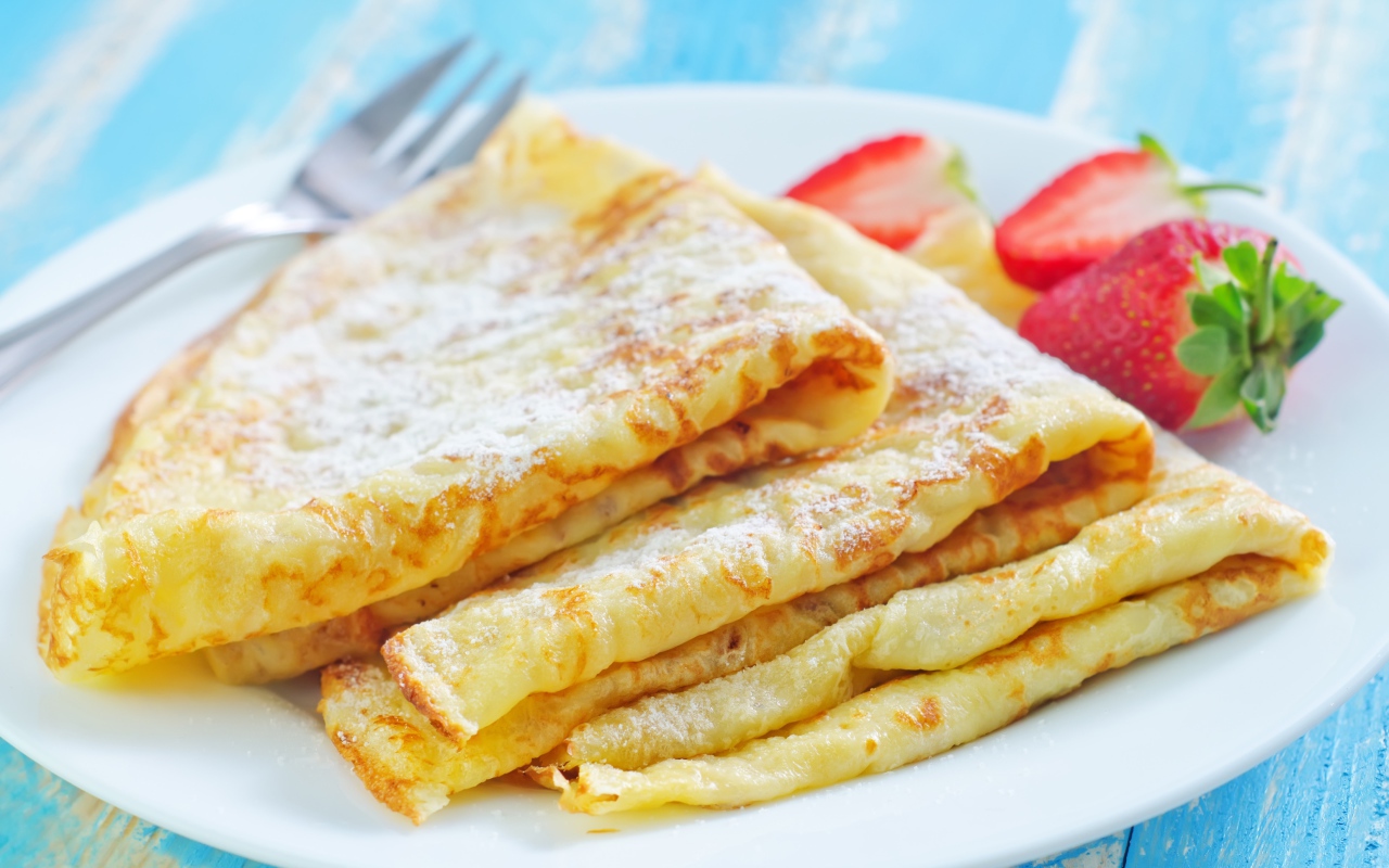 Румяные тонкие блинчики на тарелке с клубникой 